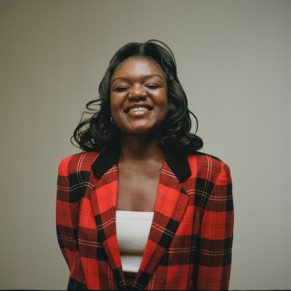Photo of woman in front of green-gray background with red flannel shirt and wavy black hair.